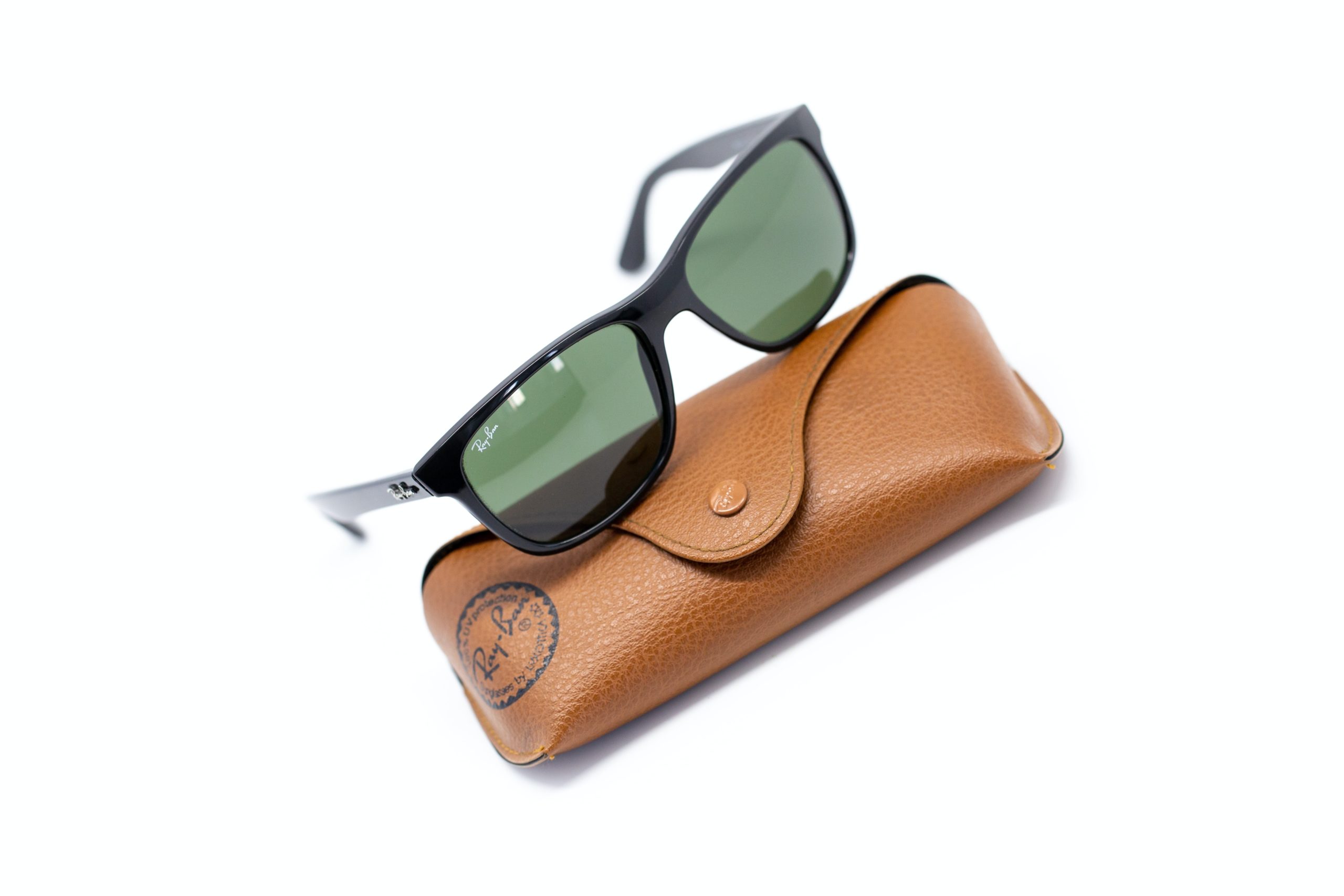 ray ban sunglasses sitting on leather case on white background